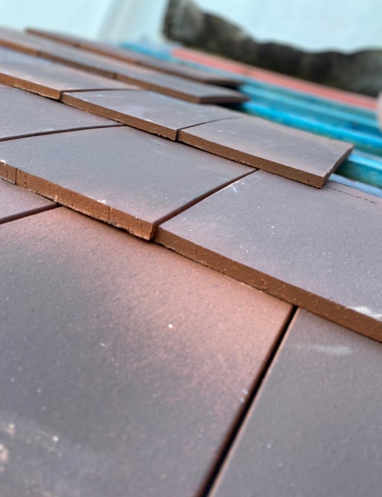Close-up of overlapping reddish-brown clay roof tiles being laid onto battens