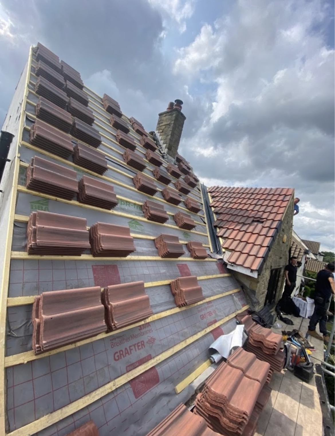 Reddish-brown profiled tiles staged on timber battens over grey breather membrane during a re-tiling job