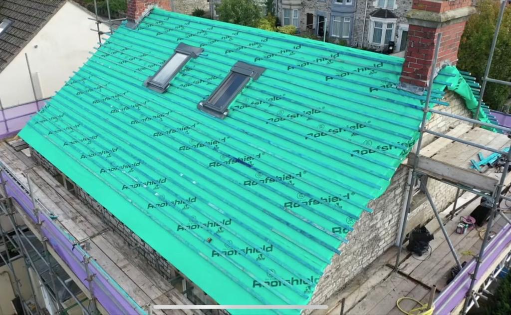 Pitched roof covered in green breathable membrane with battens and two skylights, surrounded by scaffolding