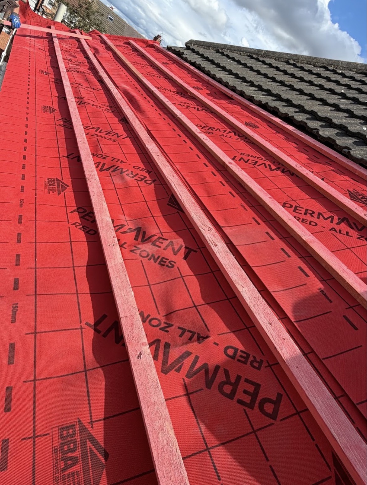 Bright red breathable underlay and timber battens being laid on a pitched roof