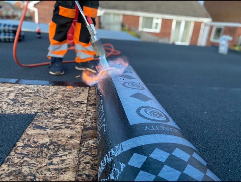 Roofer torching black bitumen felt membrane over decking on a flat roof extension