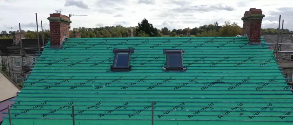 Pitched roof in green membrane with two skylights positioned between two brick chimneys