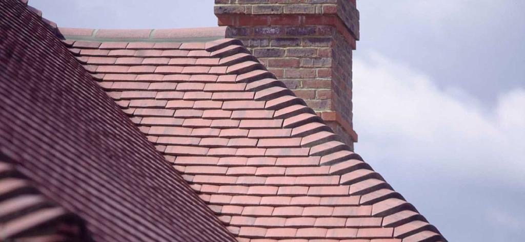 Finished pitched hip roof in reddish-brown clay plain tiles with rounded hip tiles beside a brick chimney
