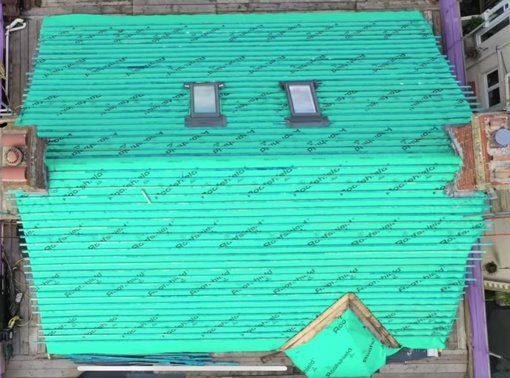 Aerial view of a full pitched and valley roof structure lined with green membrane and battens inside scaffolding