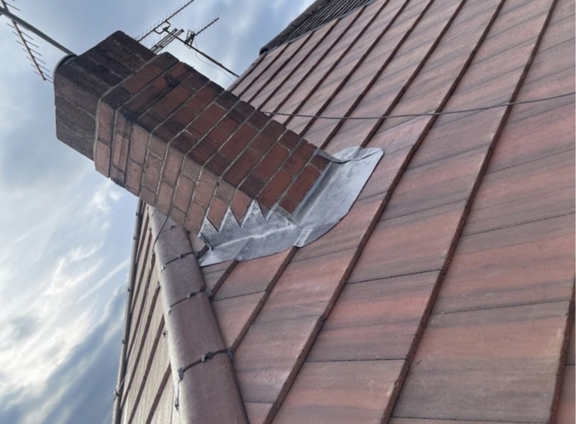 Red brick chimney stack with newly dressed stepped lead flashing over terracotta tiles
