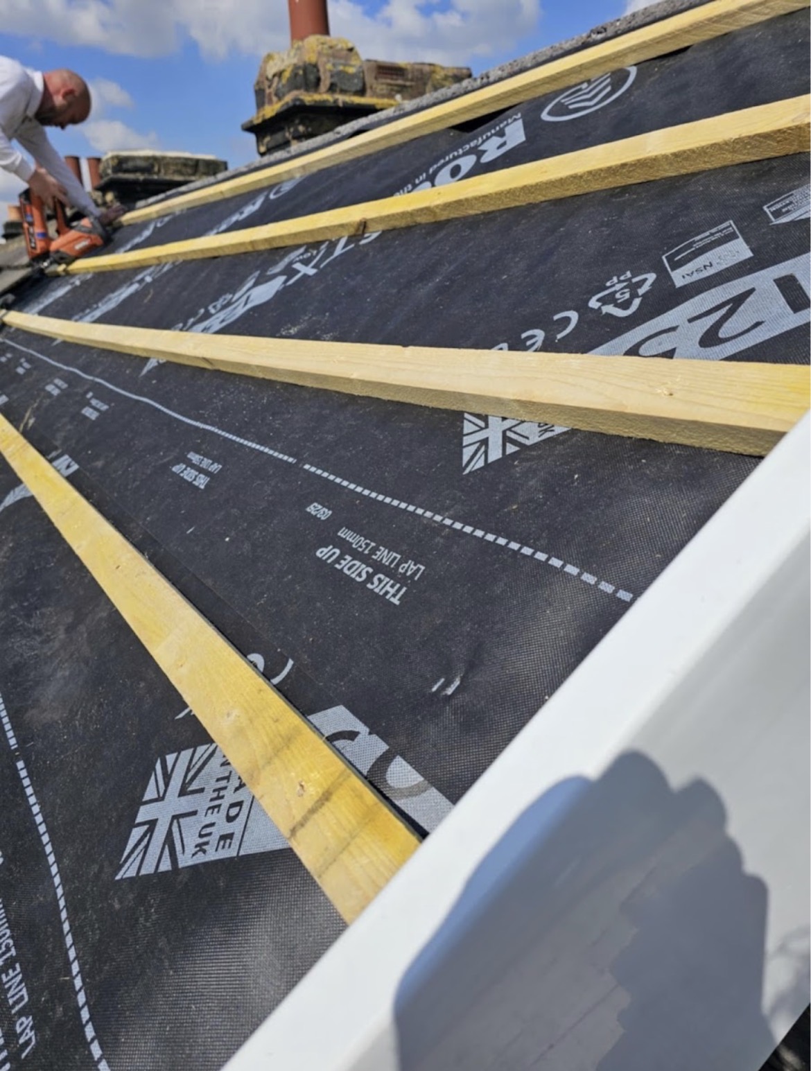 Roofer securing timber battens over black breathable membrane along a white fascia edge